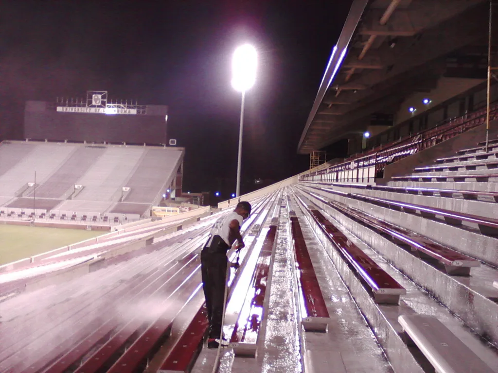 Commercial pressure washing service cleaning stadium bleachers and concrete seating - Technician power washing