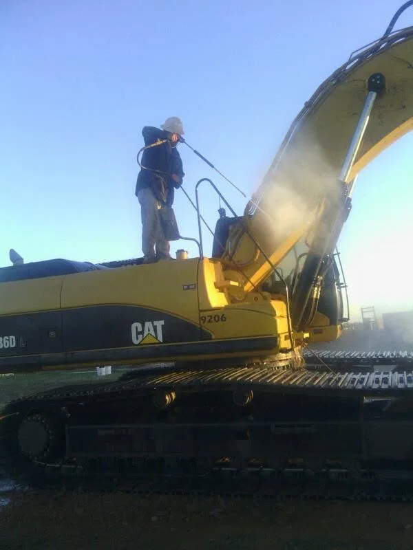 Technician standing on top of a yellow CAT excavator during a commercial pressure washing service