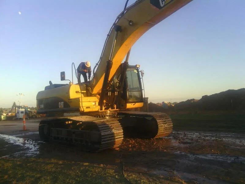 Full side view of a large CAT excavator parked on dirty ground for heavy equipment power washing