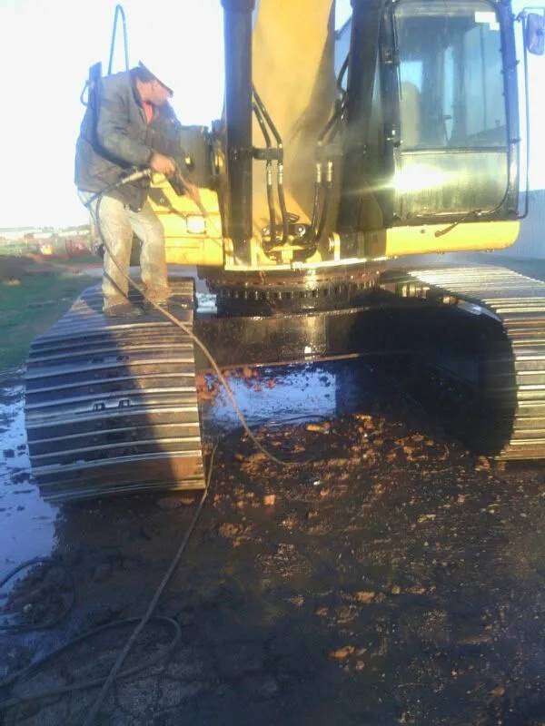 Close-up of a technician pressure washing the body and tracks of a CAT excavator