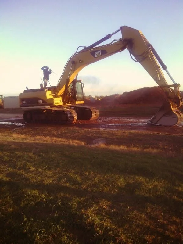 Full side view of a large CAT excavator parked on dirty ground for heavy equipment power washing